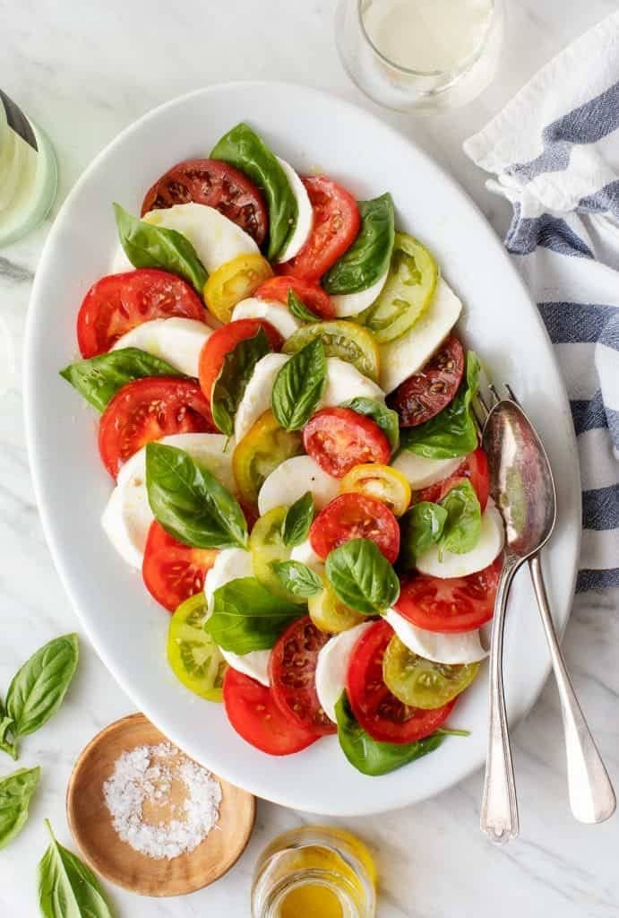 Caorese salad on an oval plate with tomatoes, basil, fresh mozzarella drizzled with oil.