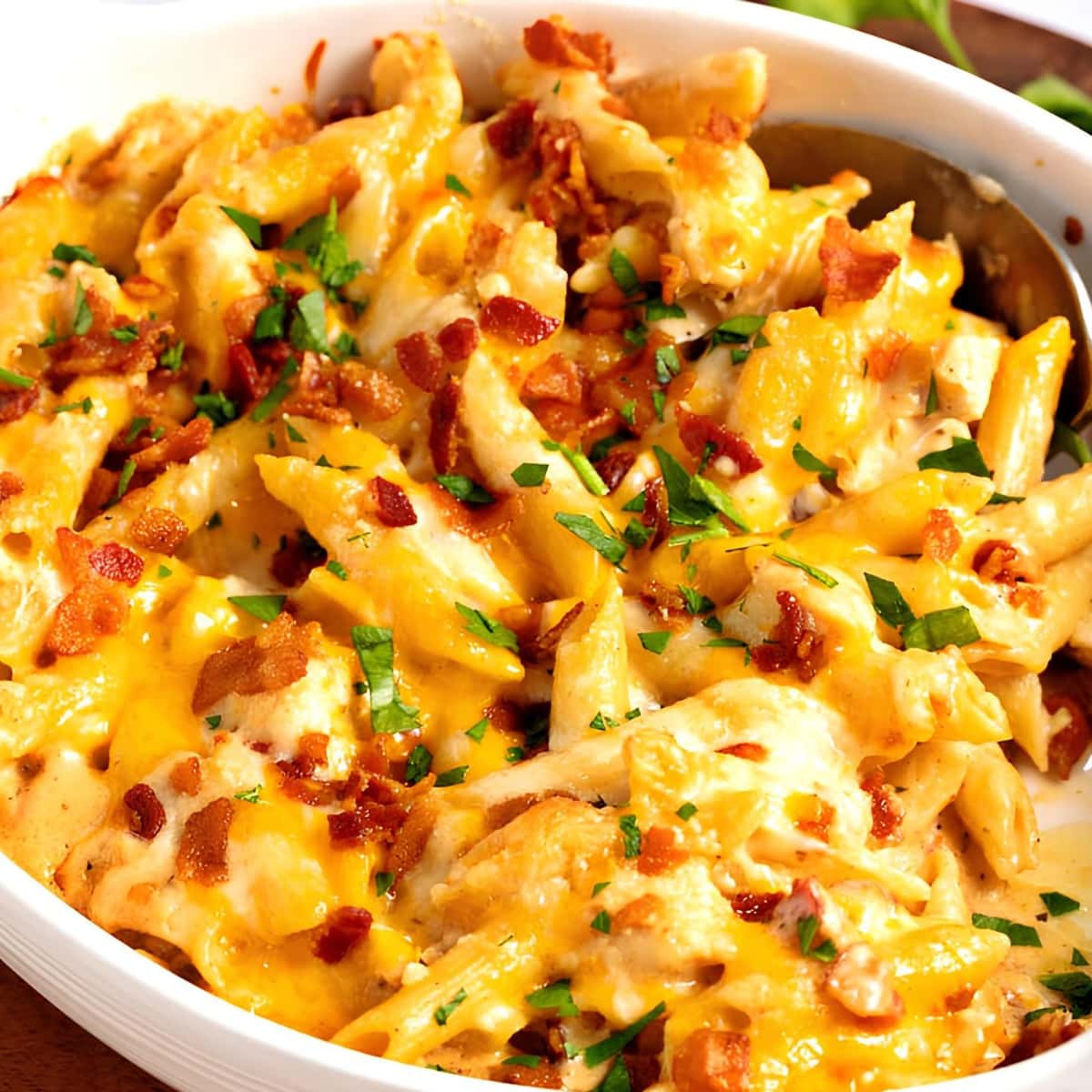 Spoon tossing chicken and bacon casserole with penne pasta on a baking dish. 