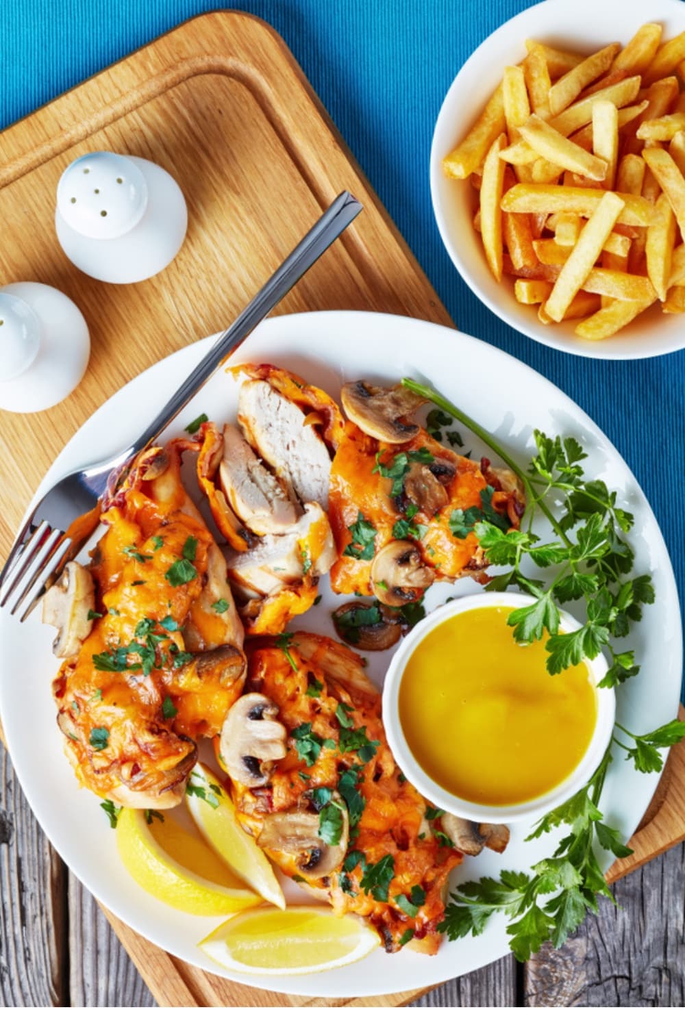 Baked chicken breast with honey mustard sauce, bacon and mushroom toppings served with sauce garnished with parsley leaves and a serving of fries on the side.