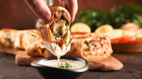 A person dipping a piece of shawarma into a small bowl of creamy sauce