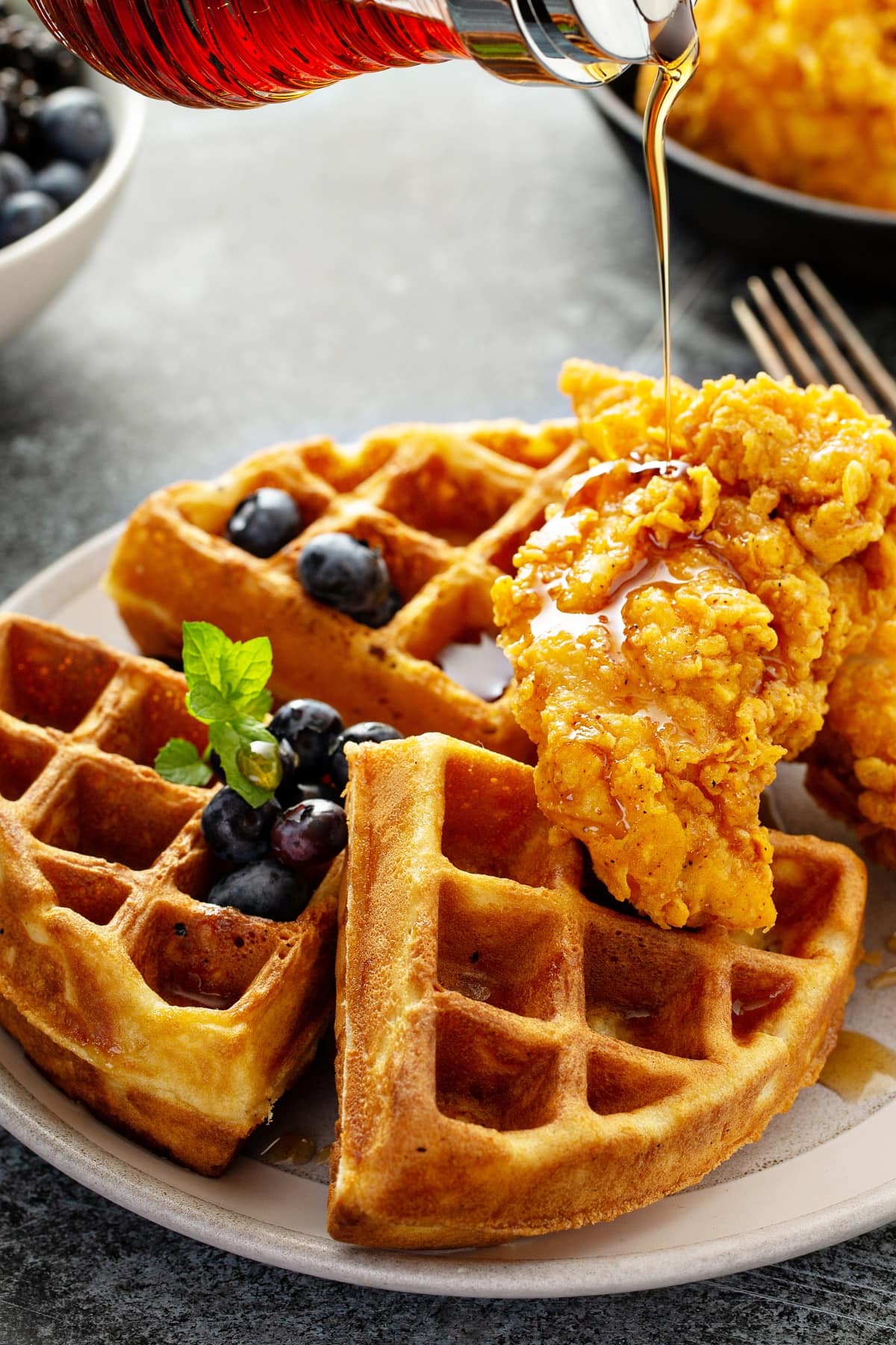 A plate of golden waffles adorned with a generous serving of fresh blueberries and crispy chicken