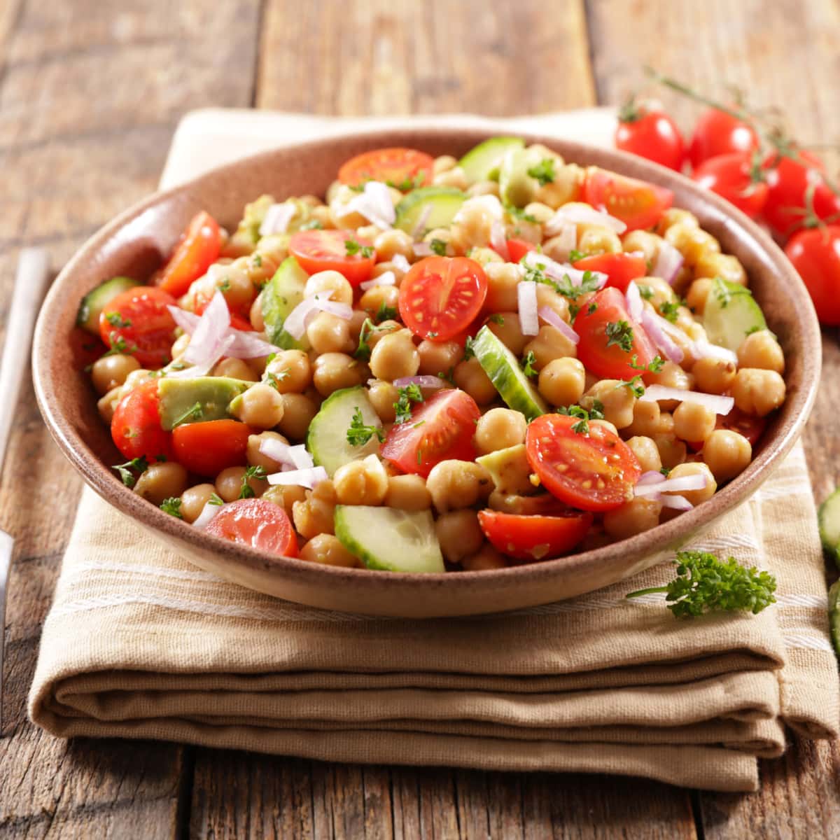 Chickpea salad in a wooden bowl with  chickpeas, juicy tomatoes, crunchy cucumbers, creamy avocado. 