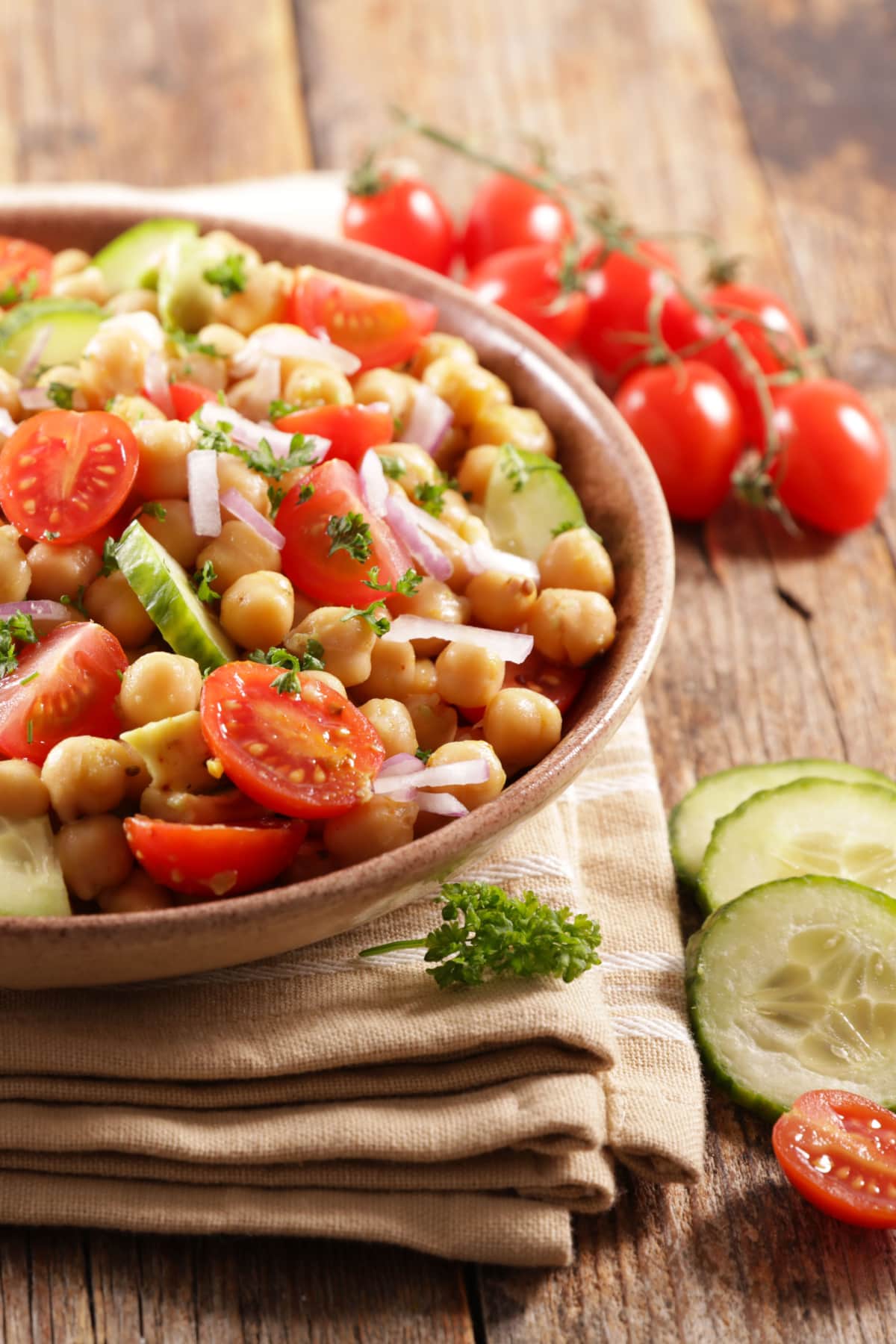 Chickpea salad made with mixed  chickpeas, juicy tomatoes, crunchy cucumbers, creamy avocado, 
 served in a wooden bowl.