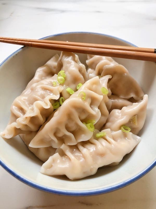 A bowl with steamed dumplings and a pair of chopsticks. 