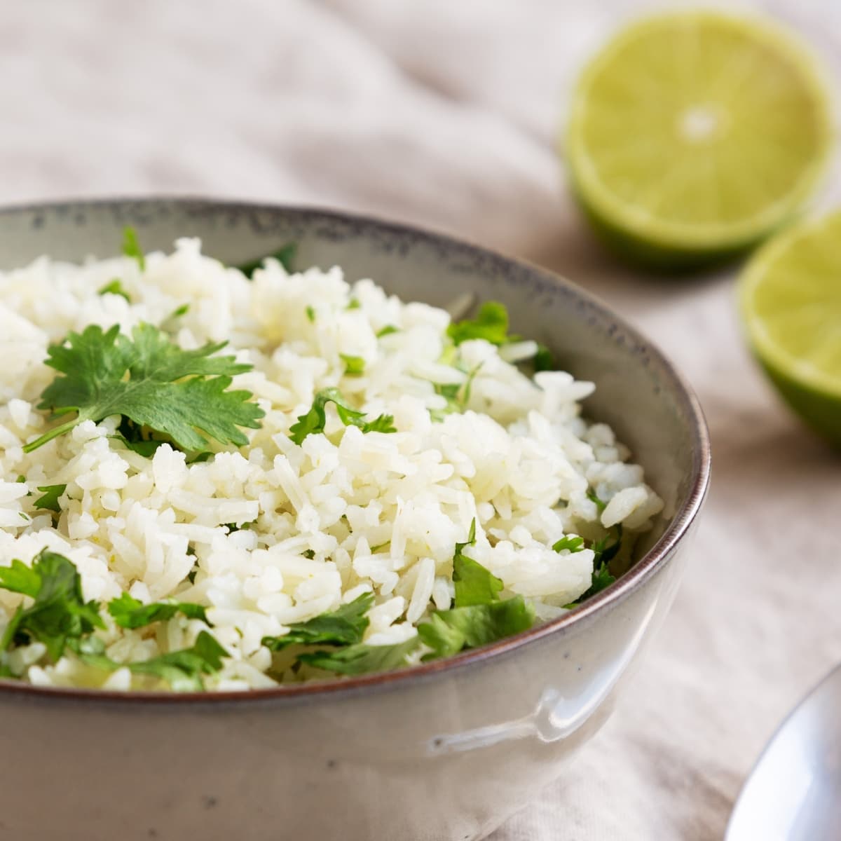 Cooked rice in a bowl garnished with cilantro beside sliced in halves lime. 