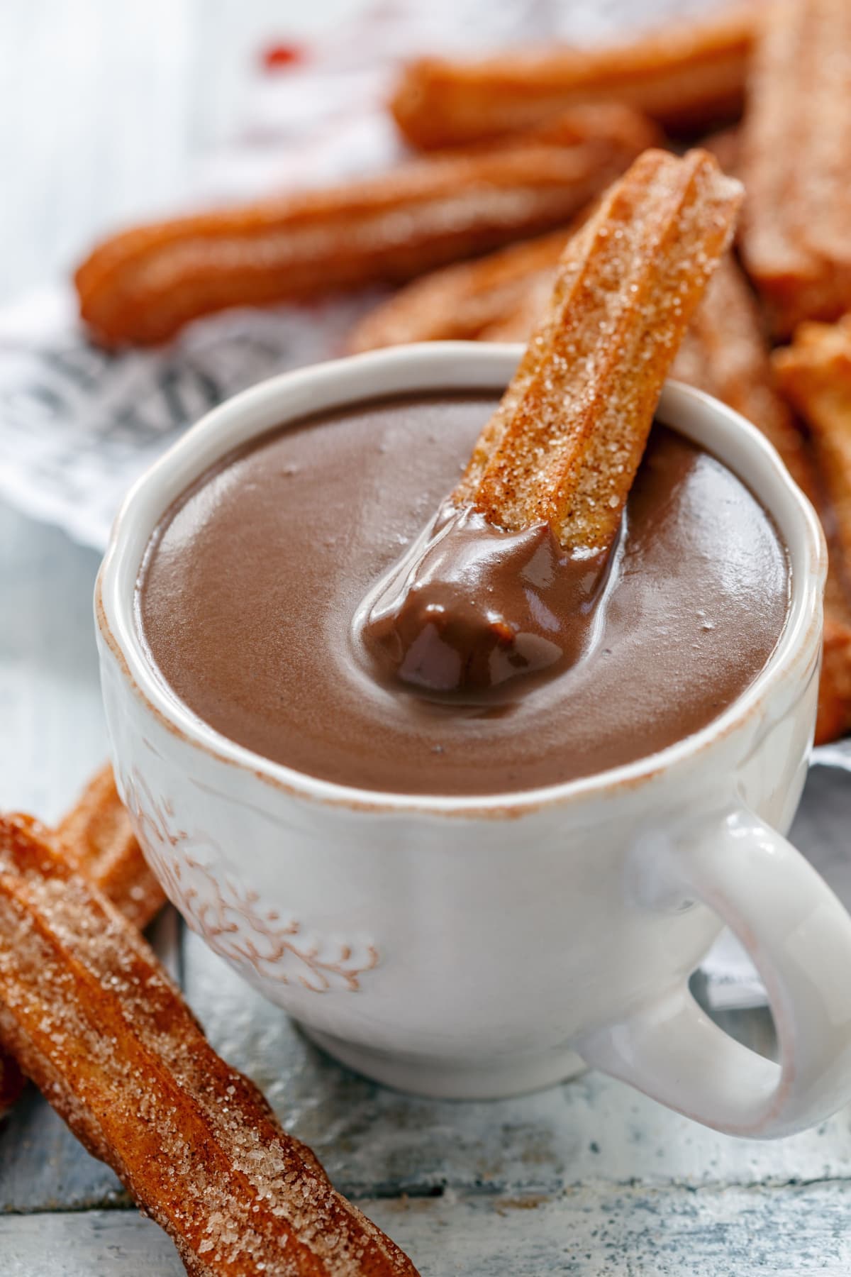 Churros coated in cinnamon sugar and one  dipped in a mug of chocolate in the classic Spanish style. 