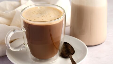 Foamy coffee on a glass mug beside a glass pitcher half filled with coconut creamer.