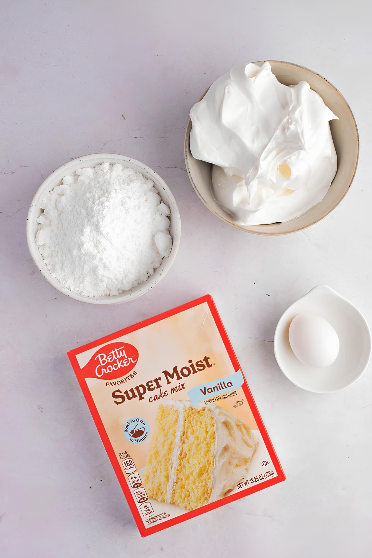 Vanilla cake mix on a box, a piece of egg, whipped cream and powdered sugar. 