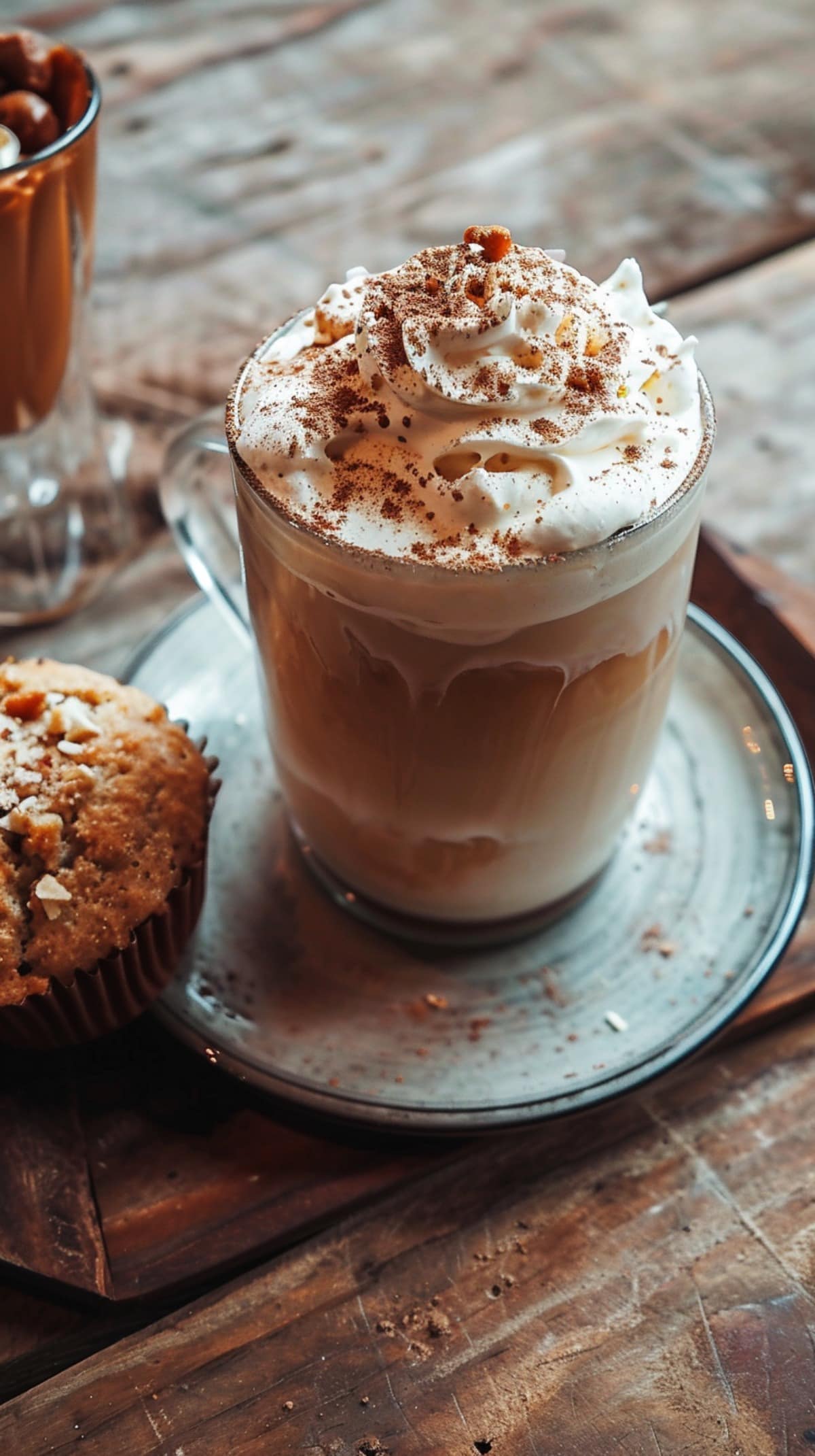 Whipped cream topped Pumpkin Spice Latte on a saucer with a muffin