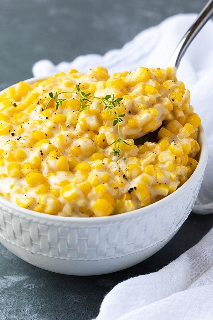 Spoon scooping a serving of creamed corn on a white bowl. 