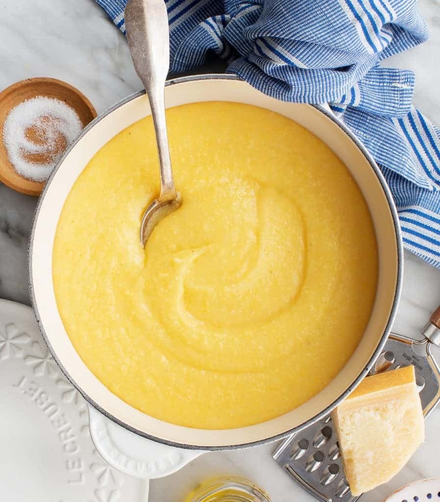 Creamy and buttery polenta on a pot mixed with a ladle.