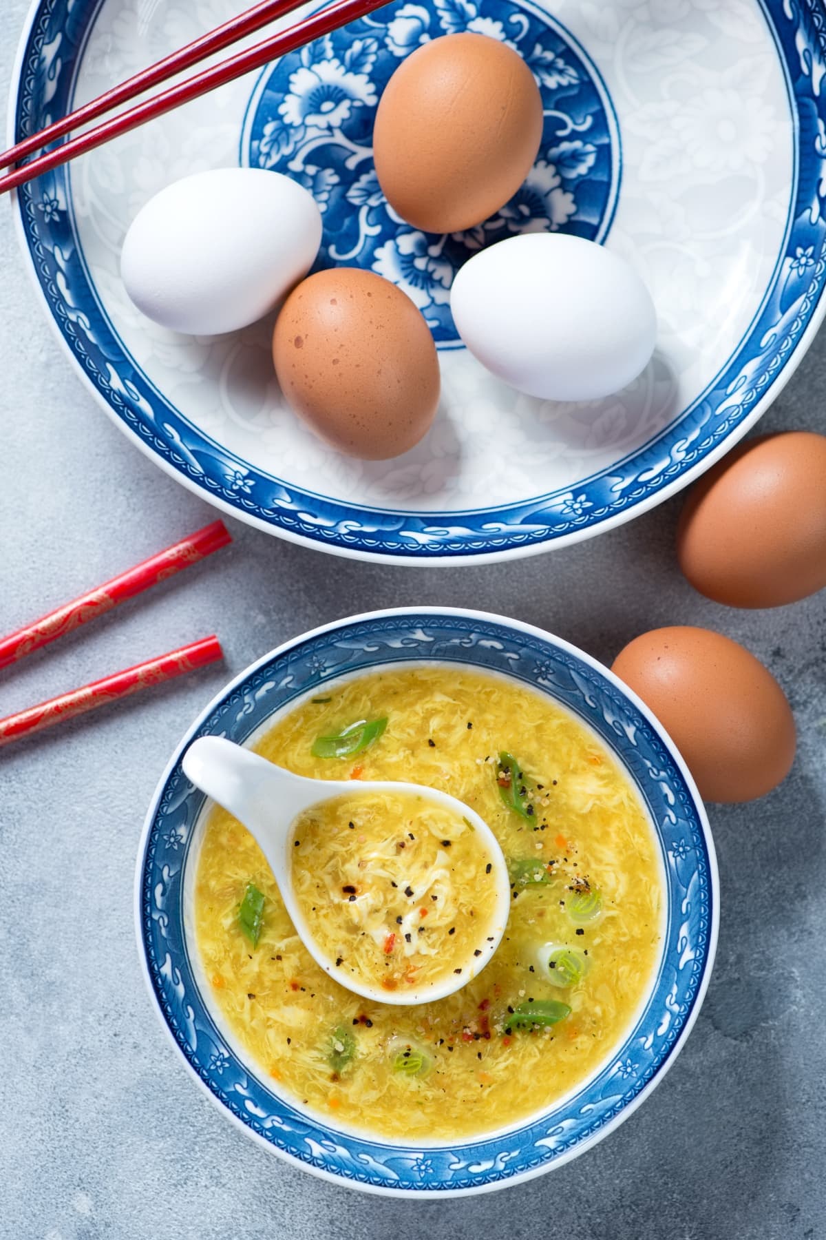 Raw brown and white eggs on a plate and a bowl of egg drop soup served in a bowl. 