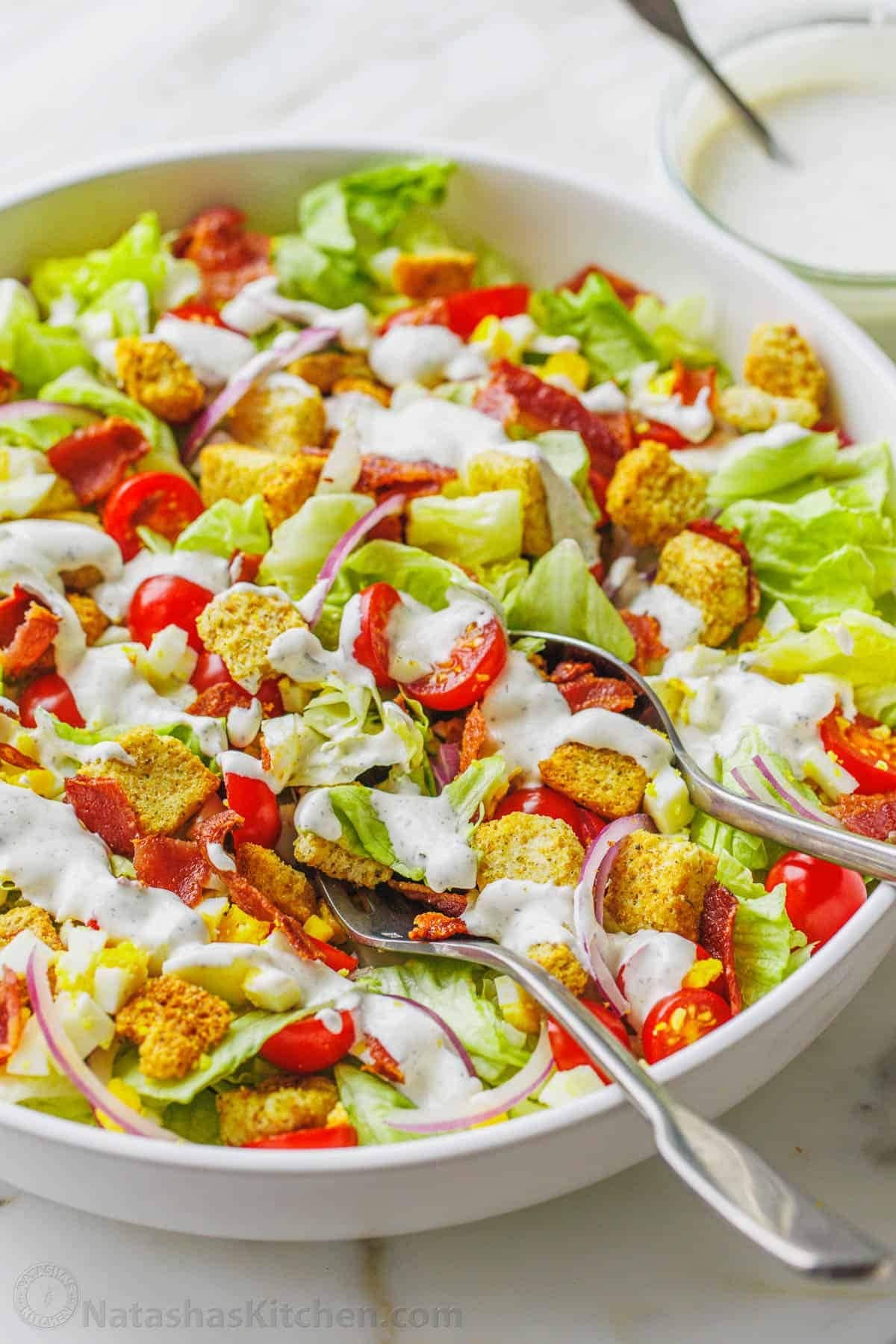 A bowl of garden salad with chopped lettuce, ripe tomatoes, a sprinkle of bacon, and homemade ranch dressing. 