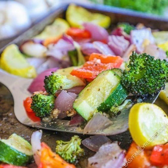 Roasted broccoli, squash, cucumber, pepper and onion tossed by a ladle on a sheet pan.