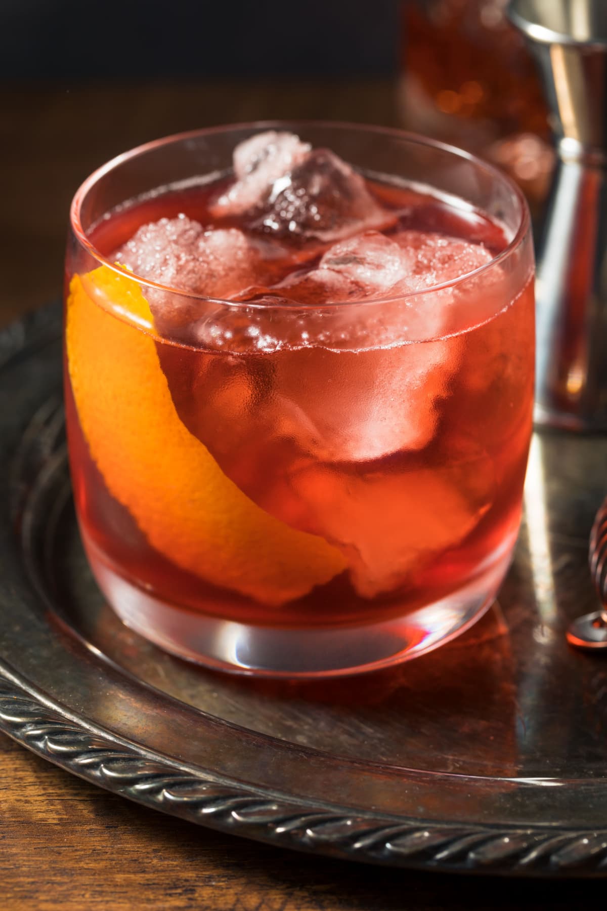A glass of Boulevardier Cocktail with ice garnished with lemon peel.