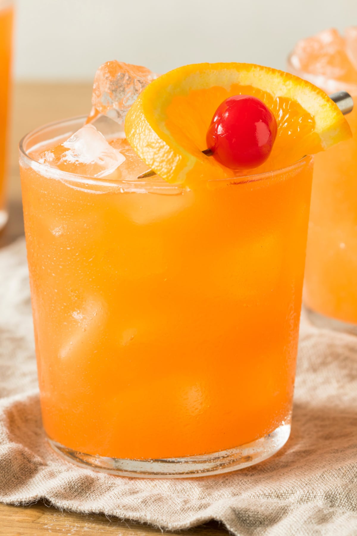 Iced cold rum swizzle served on a glass garnished with cherry and orange peel.