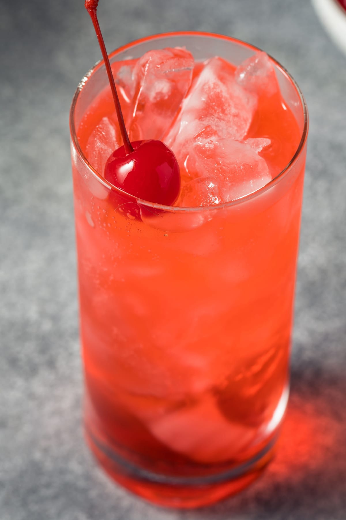 Pink Shirley Temple drink served on a tall glass filled with ice garnished with fresh cherry.