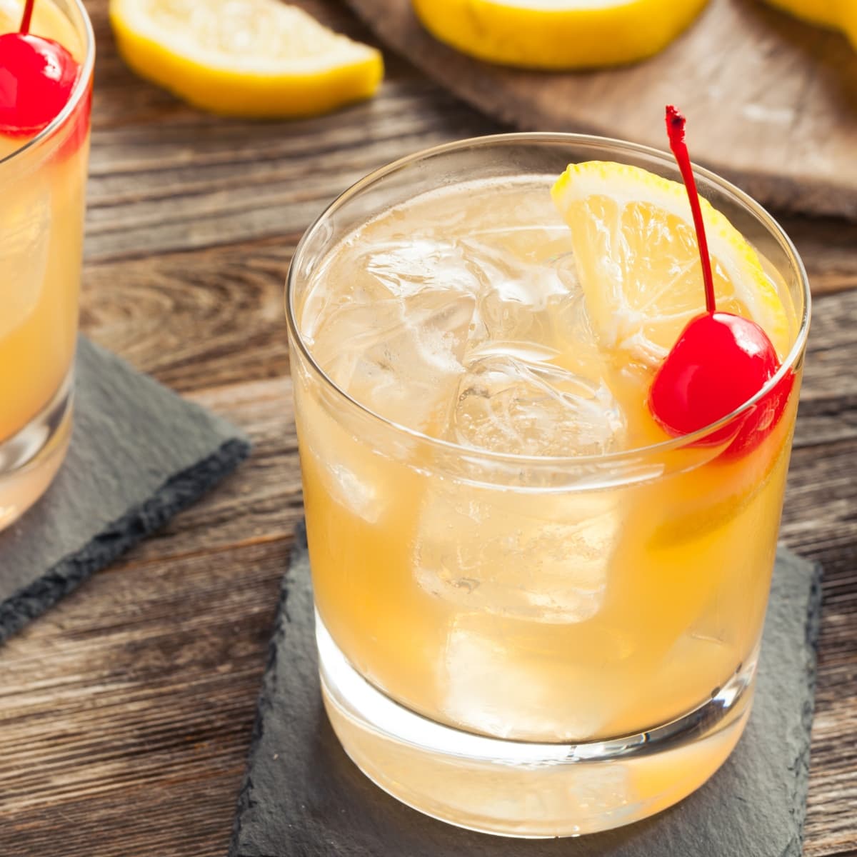 Glass of whiskey sour filled with ice topped with lemon and orange garnish. 