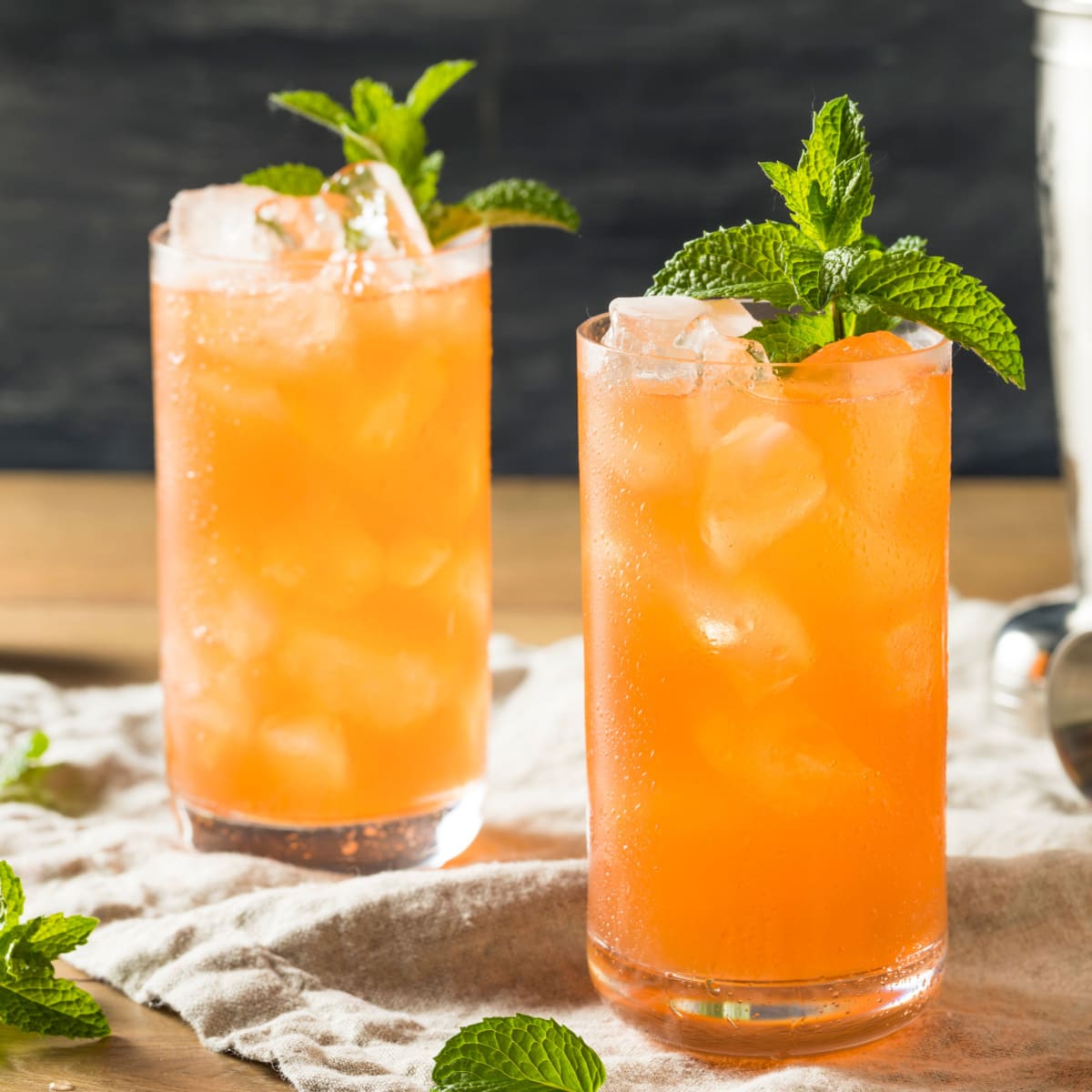 Two glasses of orangey cocktail on a tall glass filled with ice garnished with mint leaves.