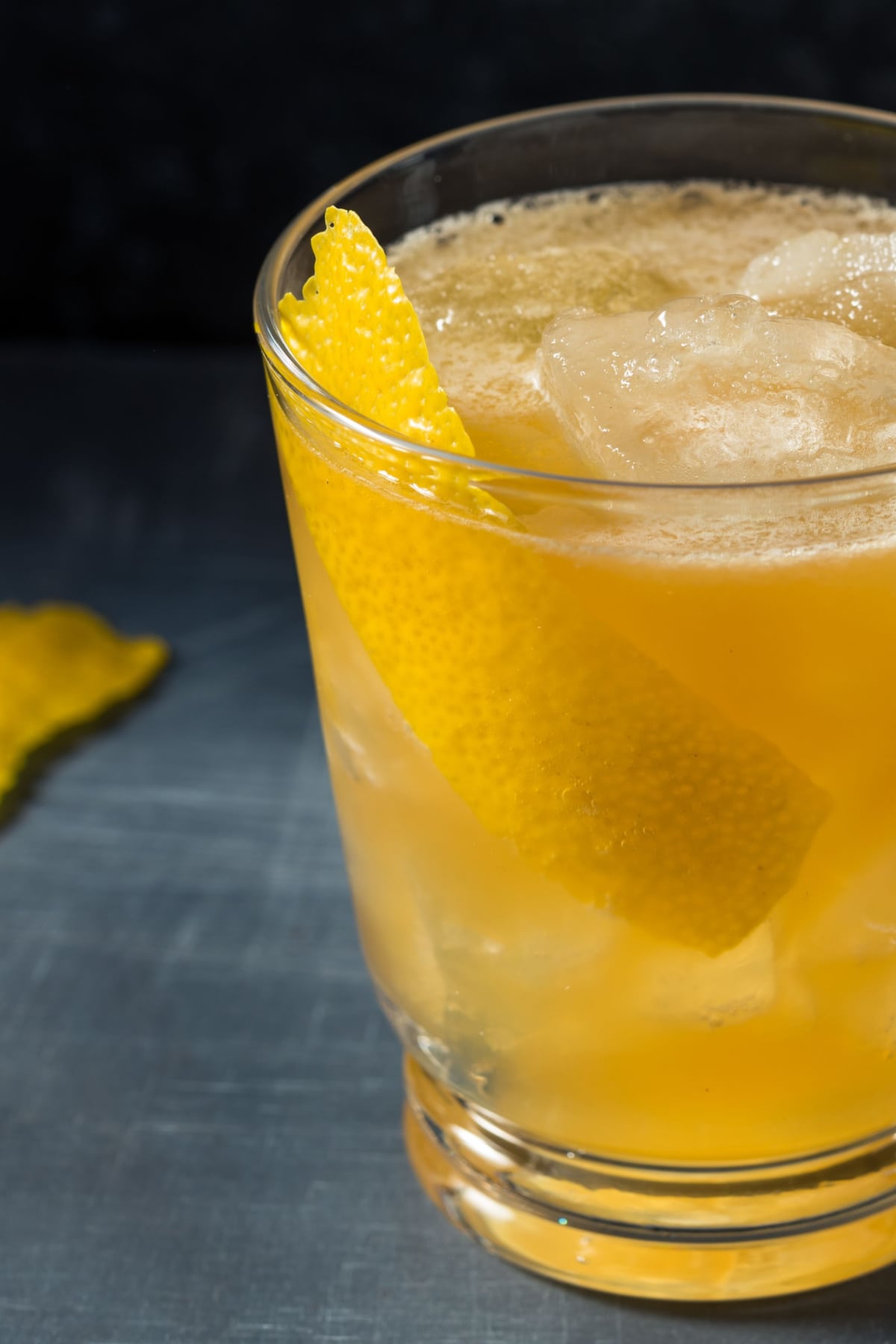 A glass of gold rush cocktail filled with ice garnished with lemon peel.