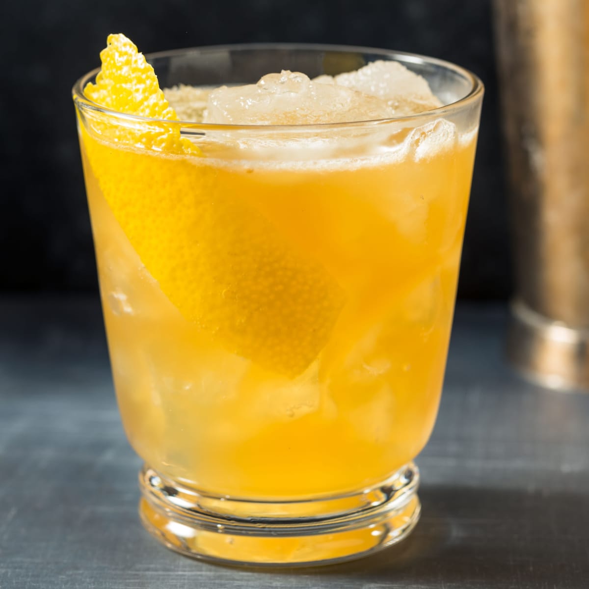 Gold rush cocktail on a glass filled with ice garnished with lemon peel. 