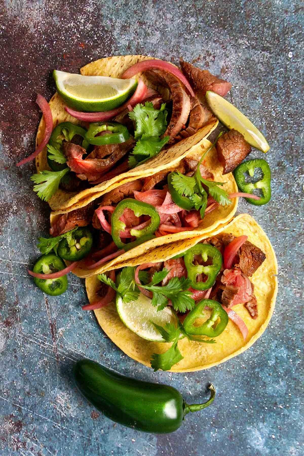 Tacos with grilled steak and sliced jalapeño and garnish with a squeeze of fresh lime, cilantro, and pickled red onions.