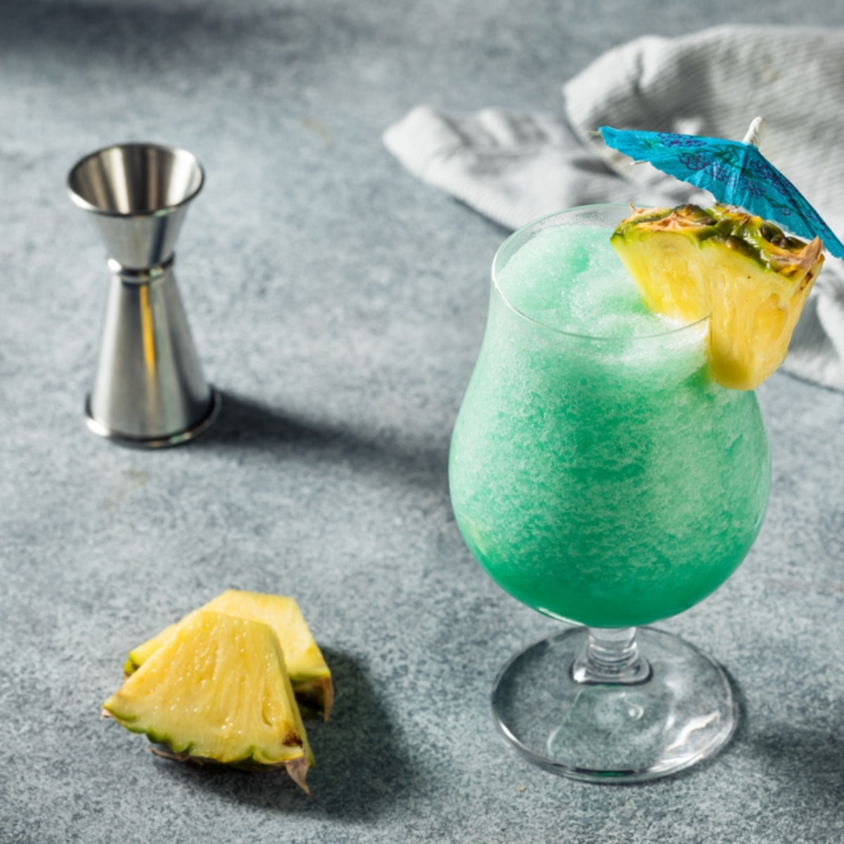 Blue Hawaiian Cocktail garnished with sliced pineapple on a concrete table.