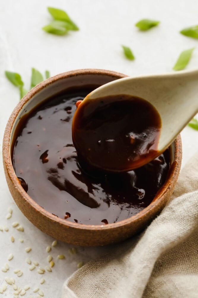 Wooden spoon dipped on a bowl of hoisin sauce. 