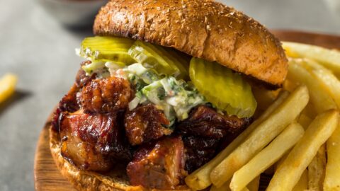 Burnt Ends Sandwich with Coleslaw and Pickles Served with Fries on a Wooden Board