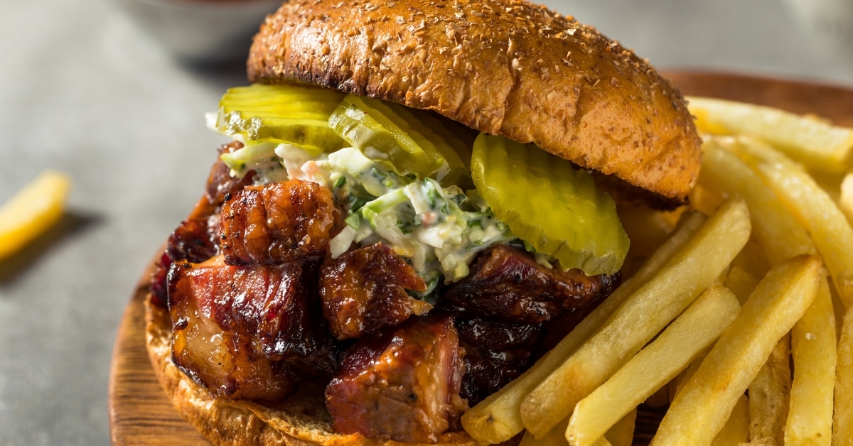 Burnt Ends Sandwich with Coleslaw and Pickles Served with Fries on a Wooden Board