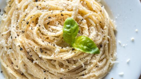 A plate of cacio e pepe topped with parmesan cheese, pepper and basil leaves