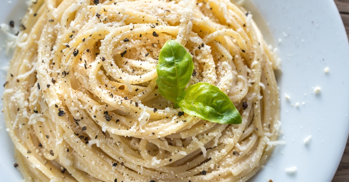 A plate of cacio e pepe topped with parmesan cheese, pepper and basil leaves