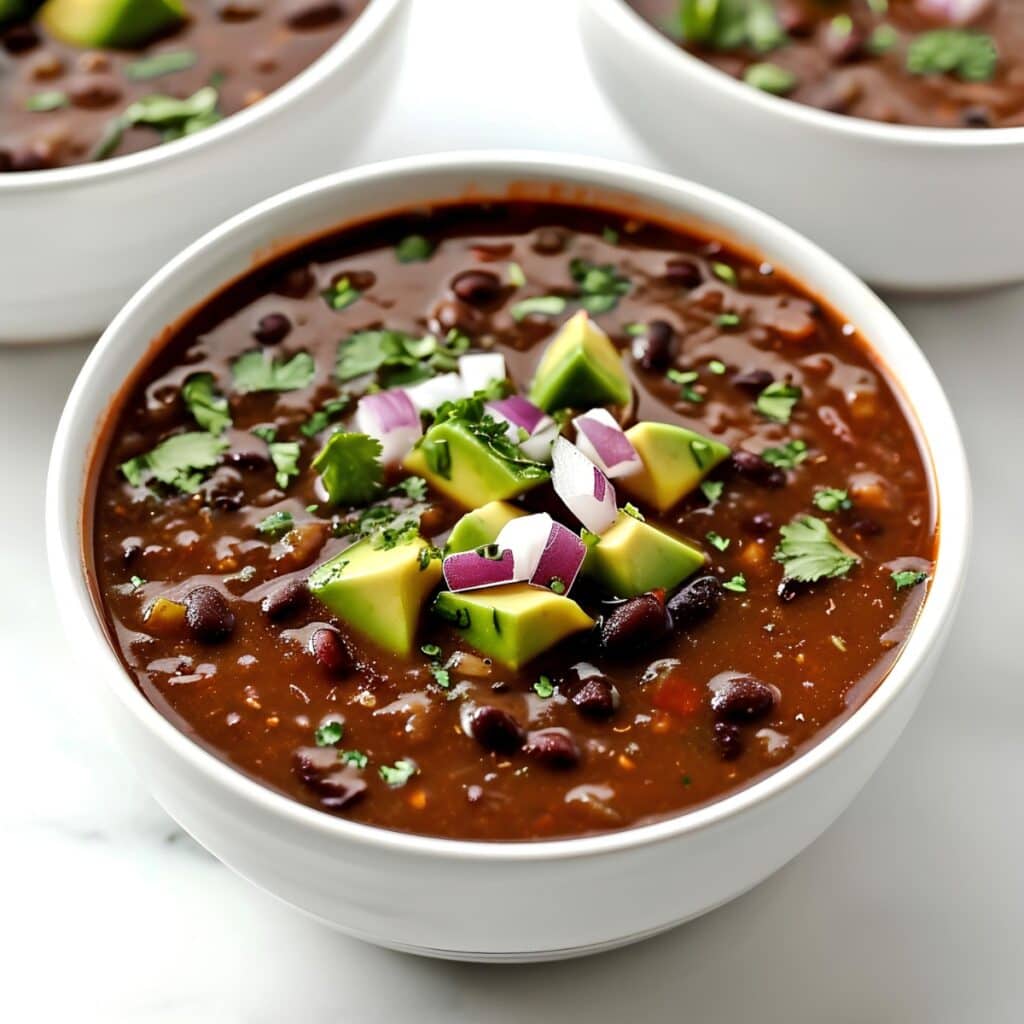 A bowl of homemade chipotle black bean soup with avocados and chopped onions