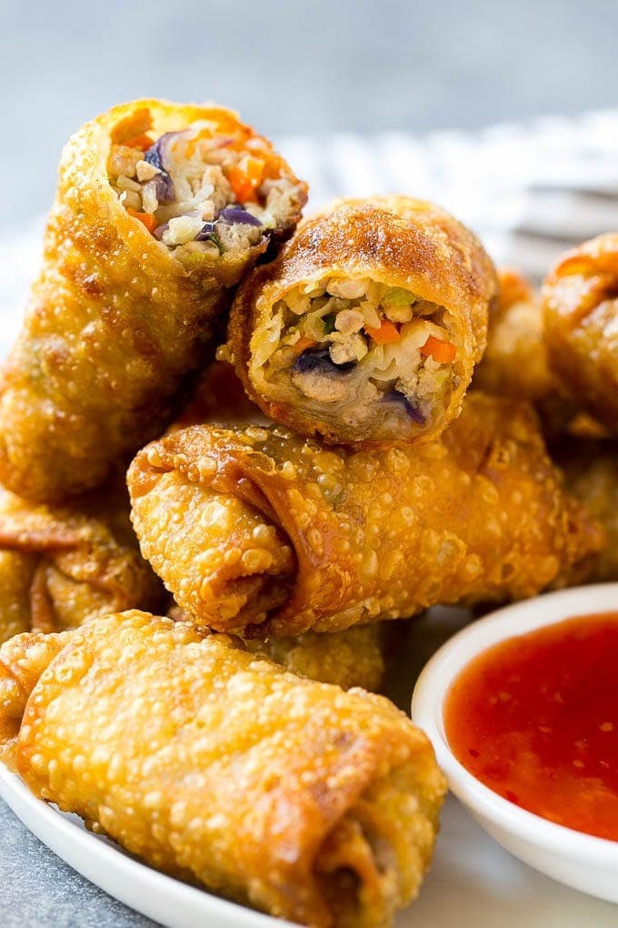 A bunch of fried egg rolls served with sweet and sour sauce.