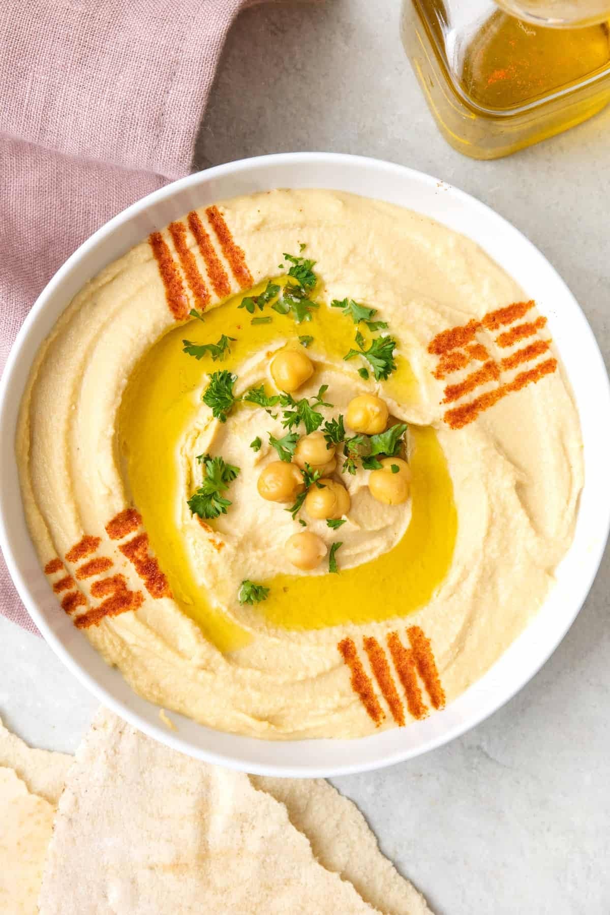 Hummus served on a white bowl garnished with chickpeas and chopped parsley leaves. 