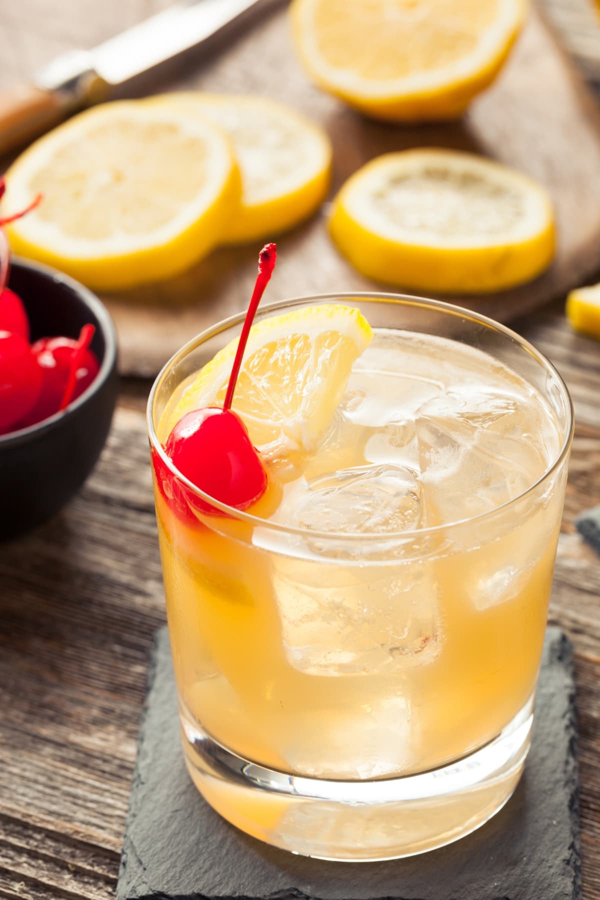 A glass of whiskey sour cocktail on a glass garnished with orange slice and cherry.