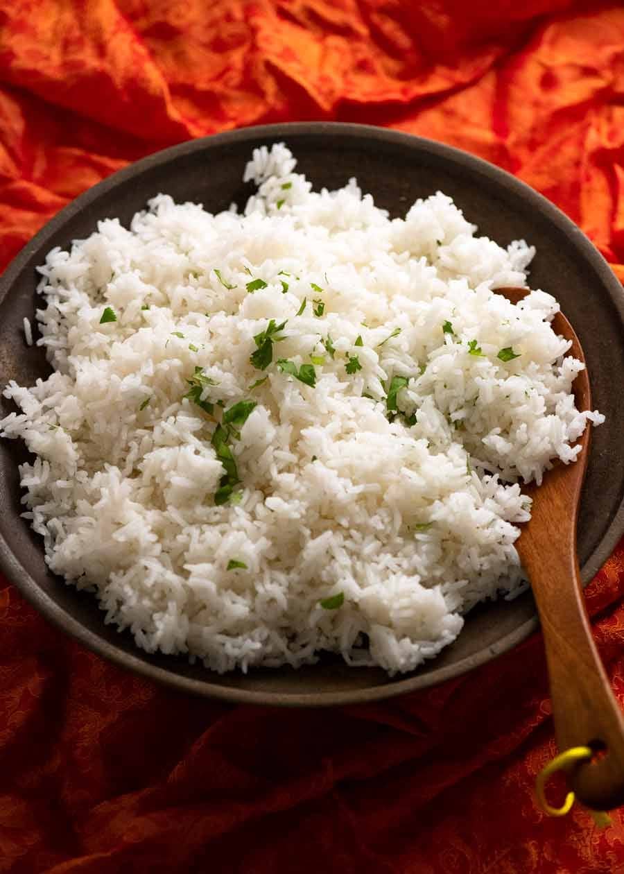 A bowl of white rice sprinkled with chopped herbs served with wooden spoon.
