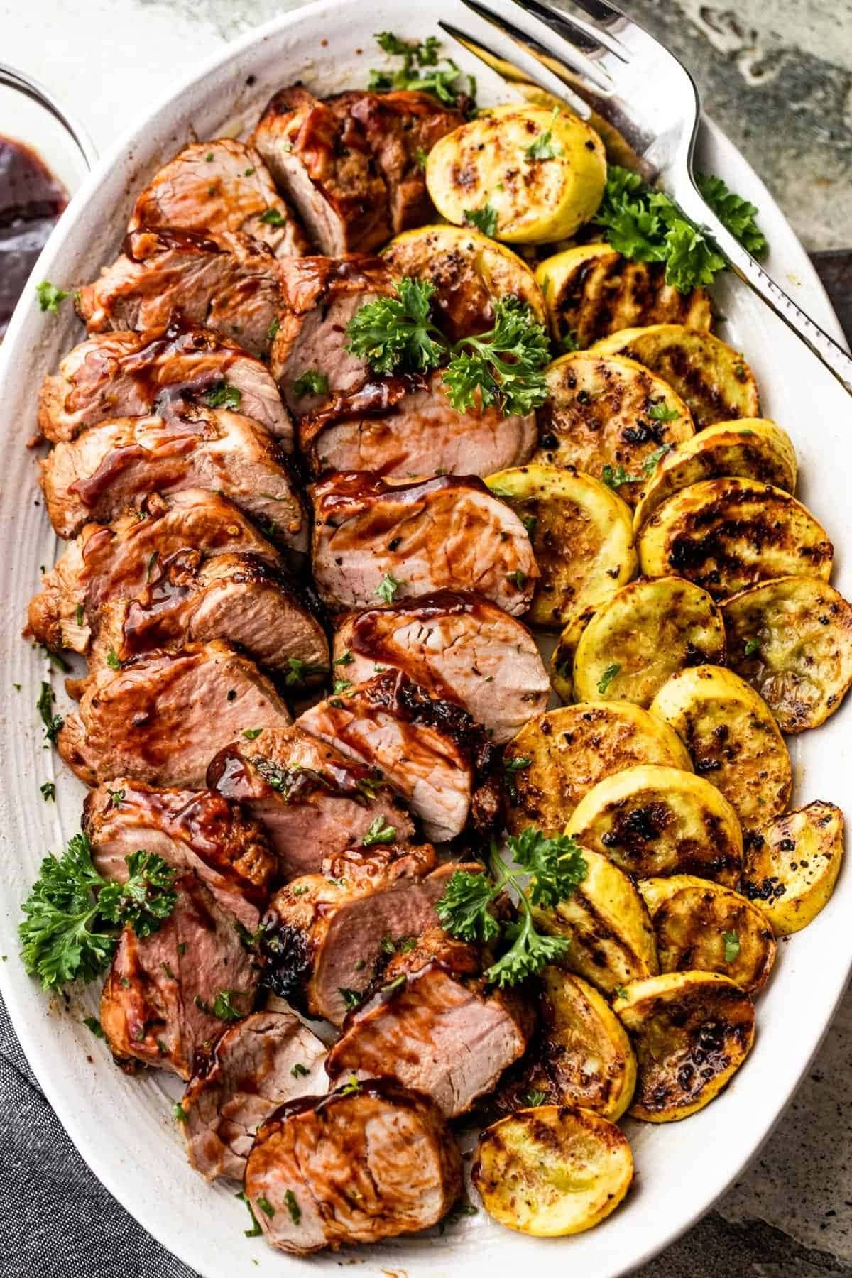 Sliced grilled pork tenderloin served with roasted sliced potatoes garnished with parsley leaves.