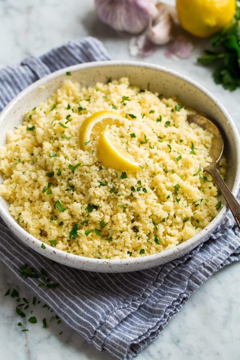 Bowl of lemon couscous garnished with chopped parsley leaves and slices of fresh lemon. 