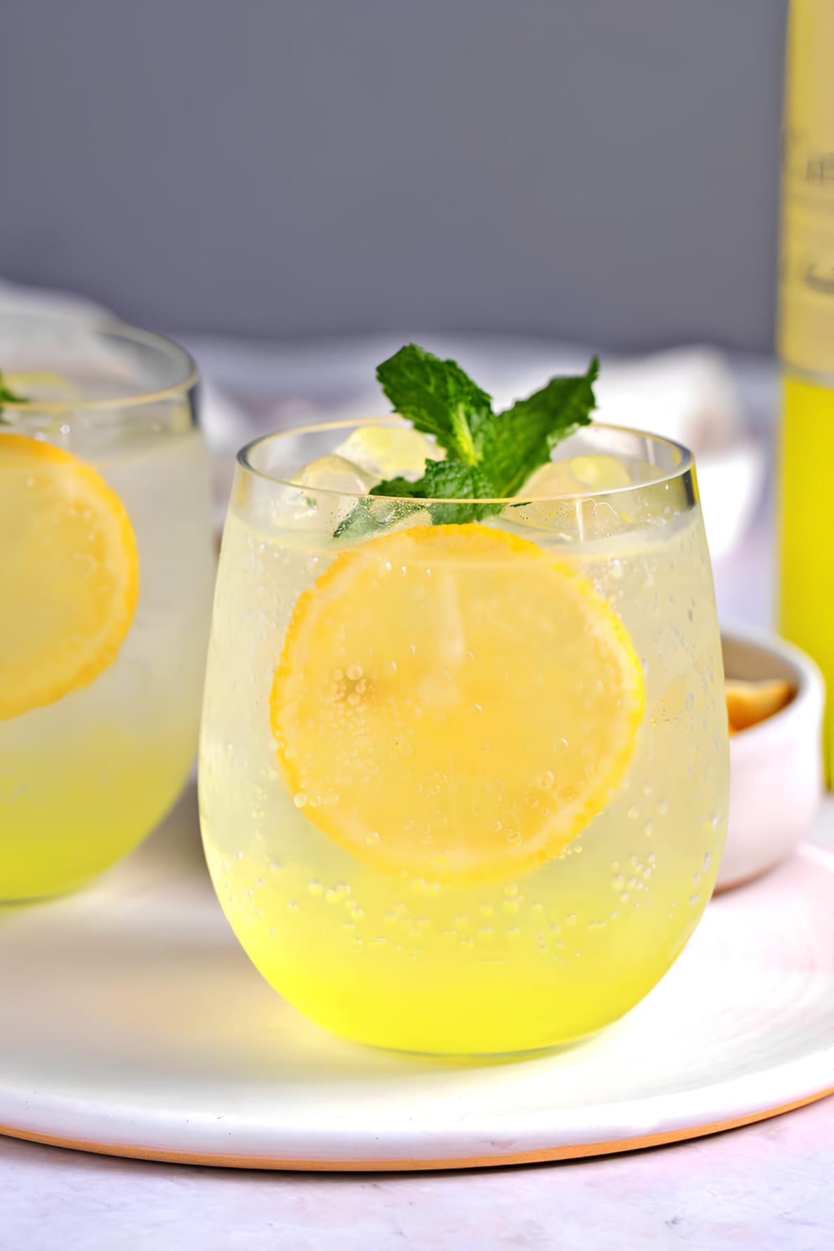 Limoncello spritz cocktail on ice garnished with slices of lemon and fresh mint sprigs served on glasses.