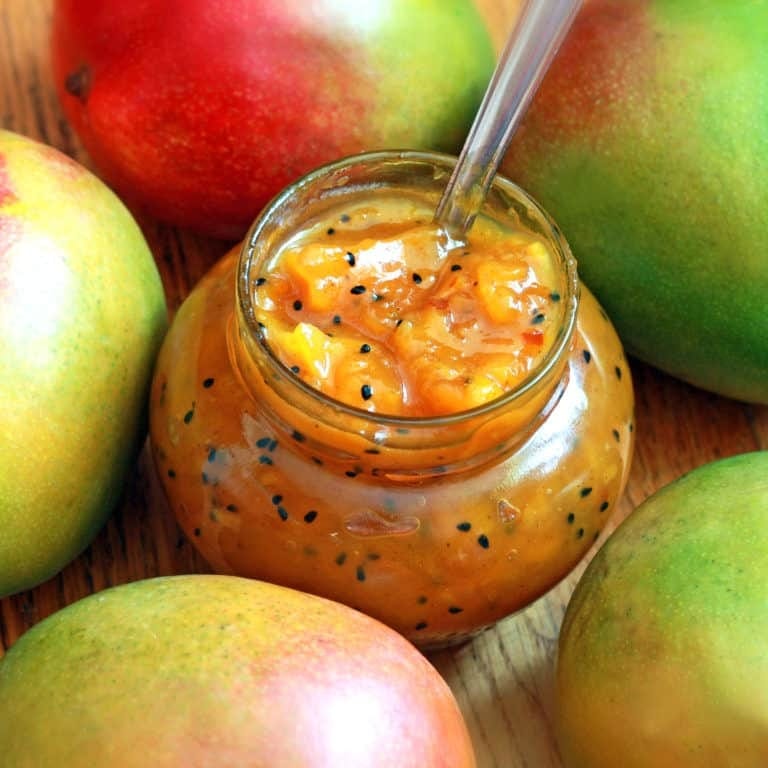 Mango chutney on a small glass jar surrounded with unripe mangoes. 