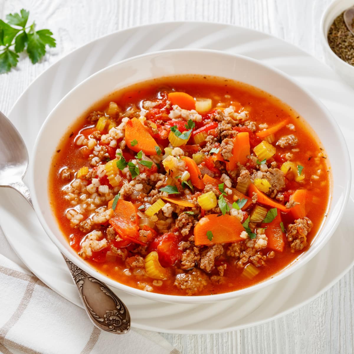 Hamburger soup in a white bowl with carrots, corn kernel, ground meat and tomato sauce. 