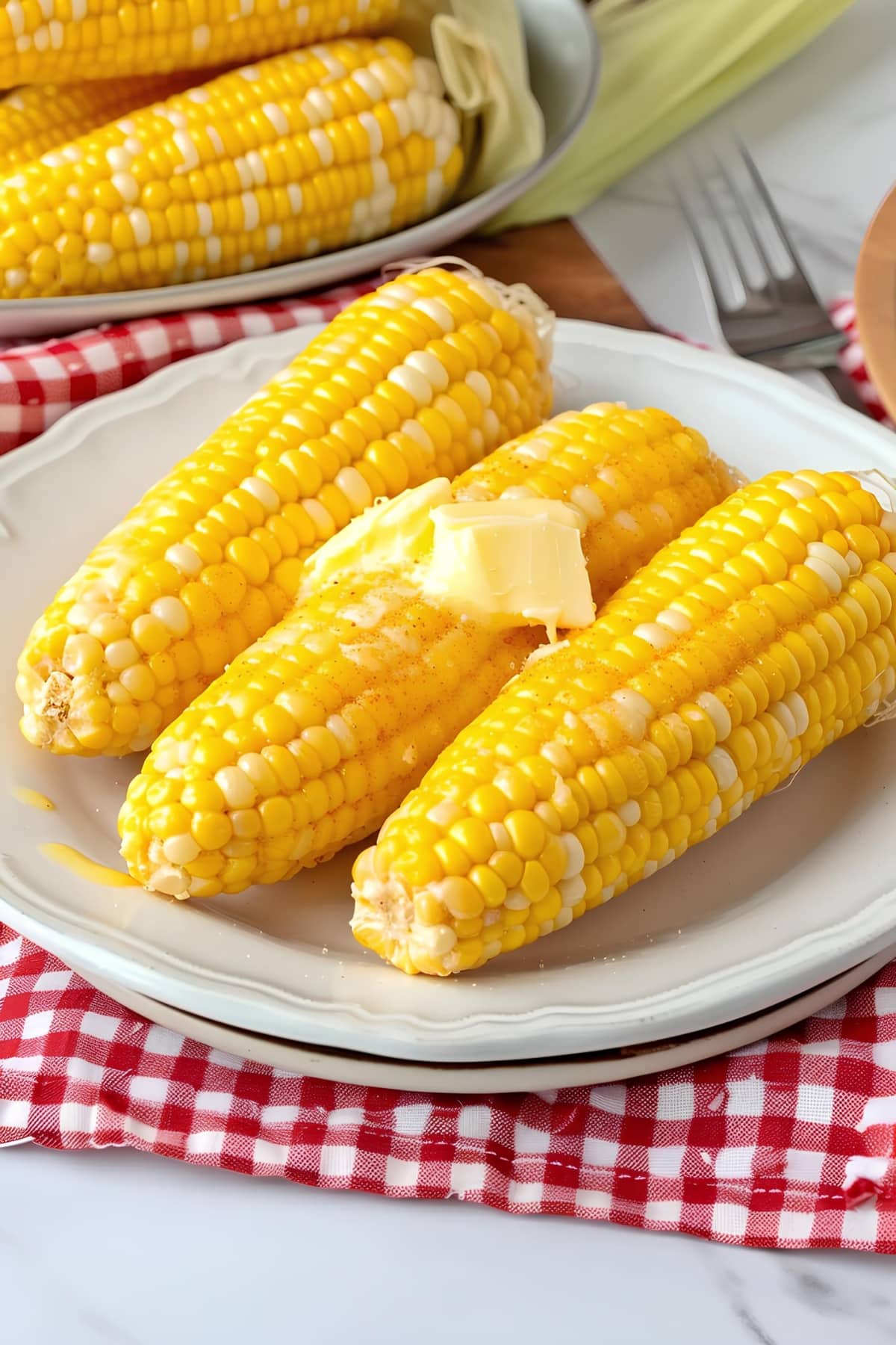 Two corn cobs on a plate, topped with a dollop of butter, ready to be enjoyed.