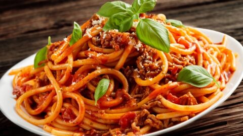 Serving of one pot spaghetti on a white plate garnished with basil leaves and parmesan cheese.