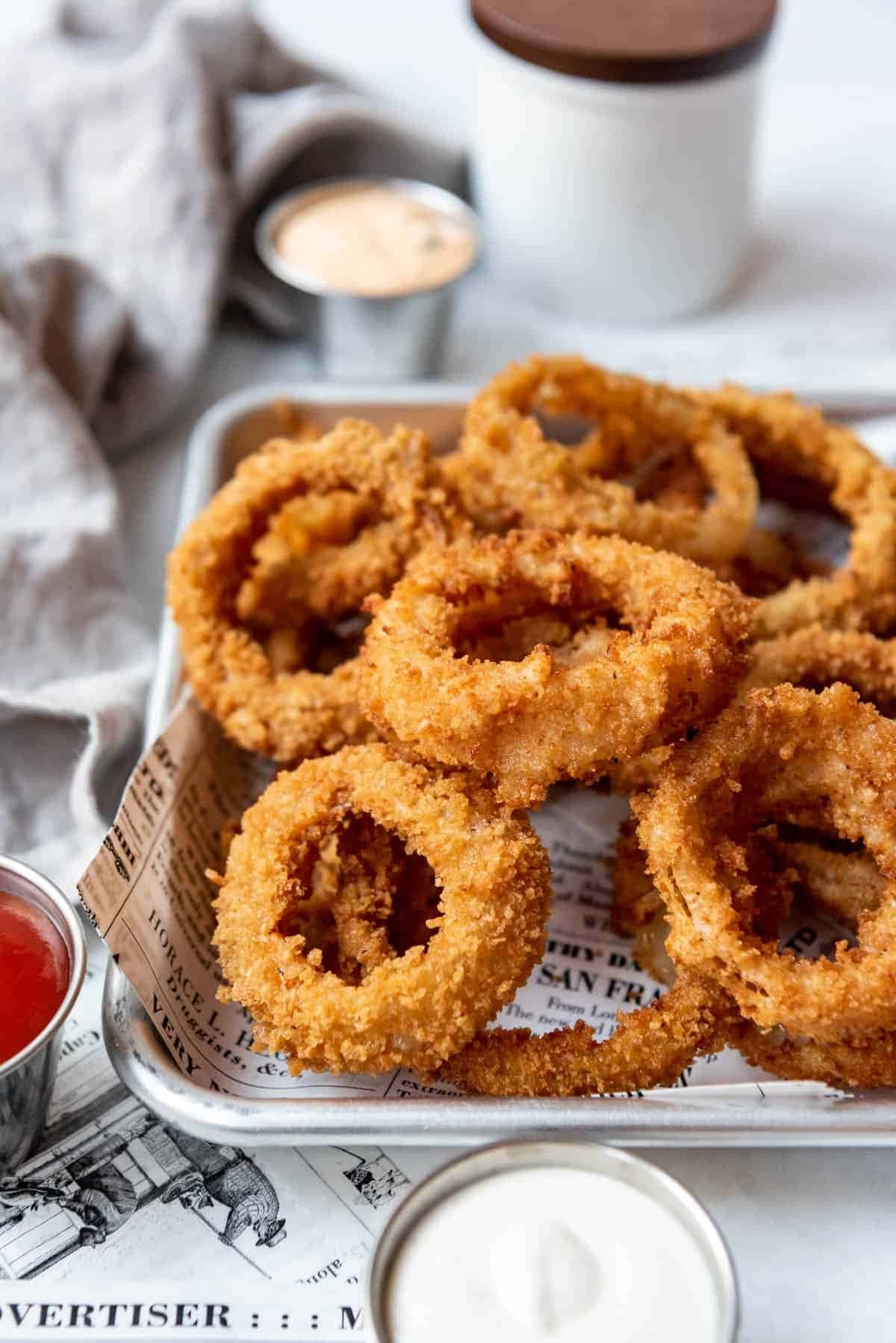 Bunch of onion rings on a baking pan with paper lining and a dipping sauce on side.
