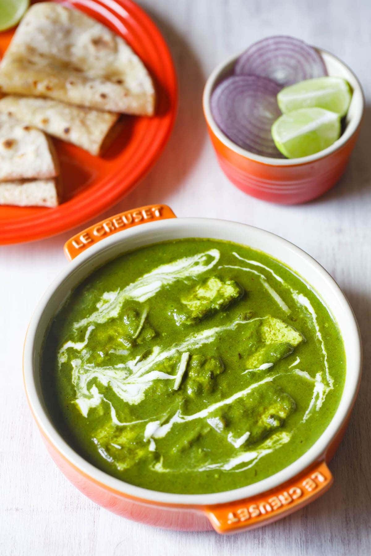 Palak paneer on an orange pot drizzled with white sauce. 