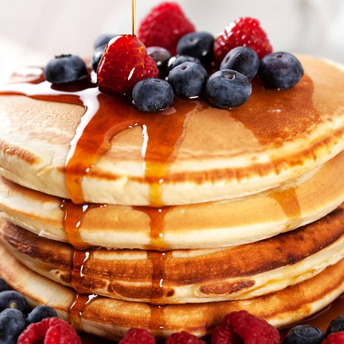 Closeup of stacked fluffy Bisquick pancakes garnished with berries drizzled with maple syrup. 