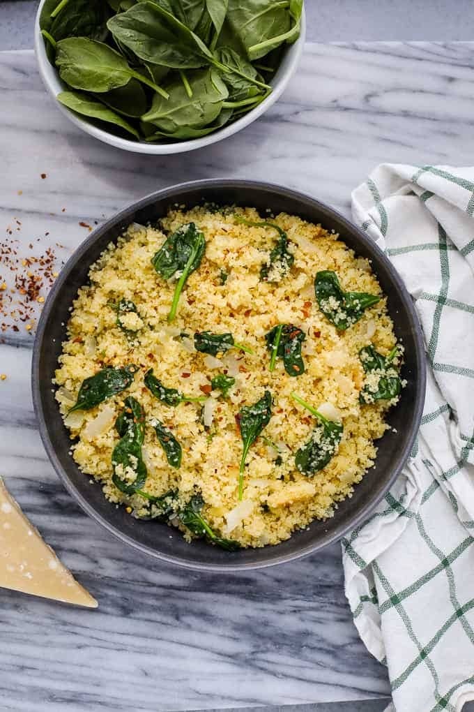Black bowl with couscous garnished with spinach and parmesan cheese.