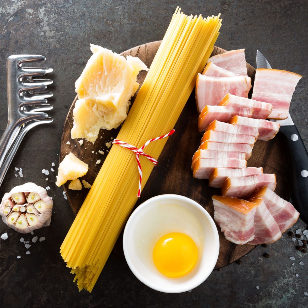 Pasta noodles, egg yolk, parmesan cheese and sliced bacon on a wooden board. 