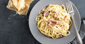 A serving of pasta carbonara with bacon and cheese on a gray plate.